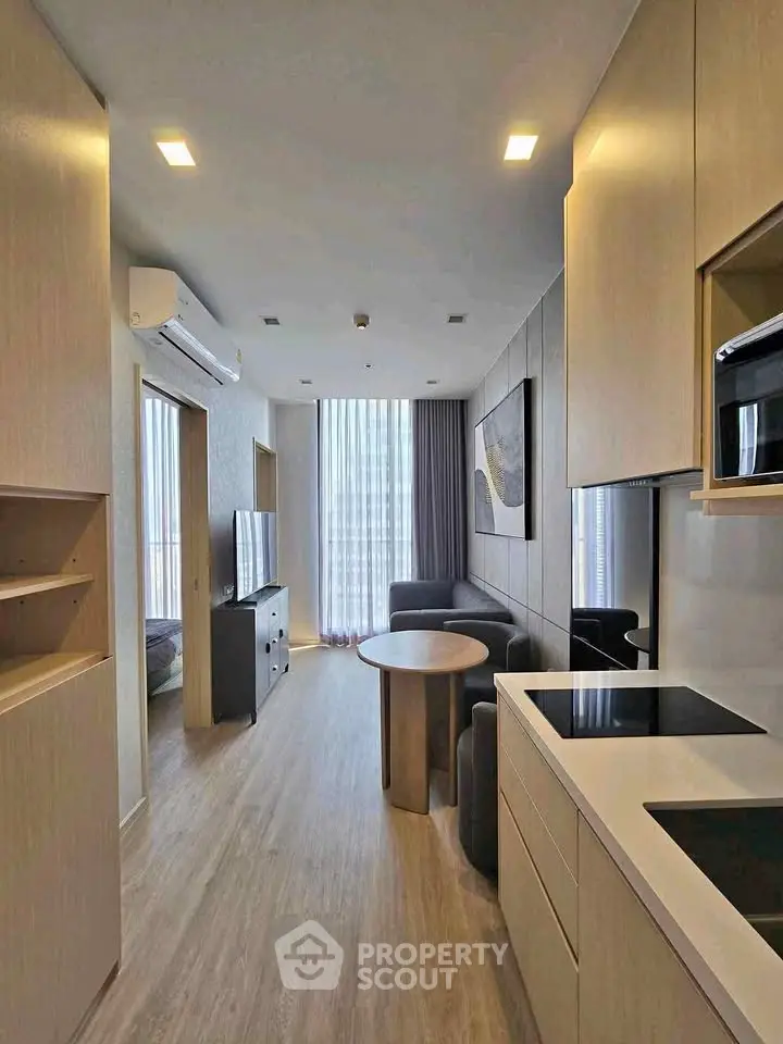 Modern open-layout living room with sleek kitchen and cozy seating area, featuring floor-to-ceiling windows.