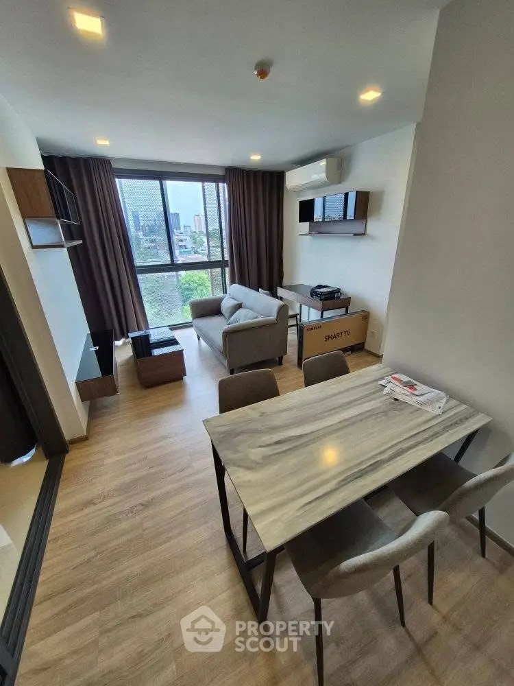Modern living room with dining area and city view, featuring sleek furniture and large windows.