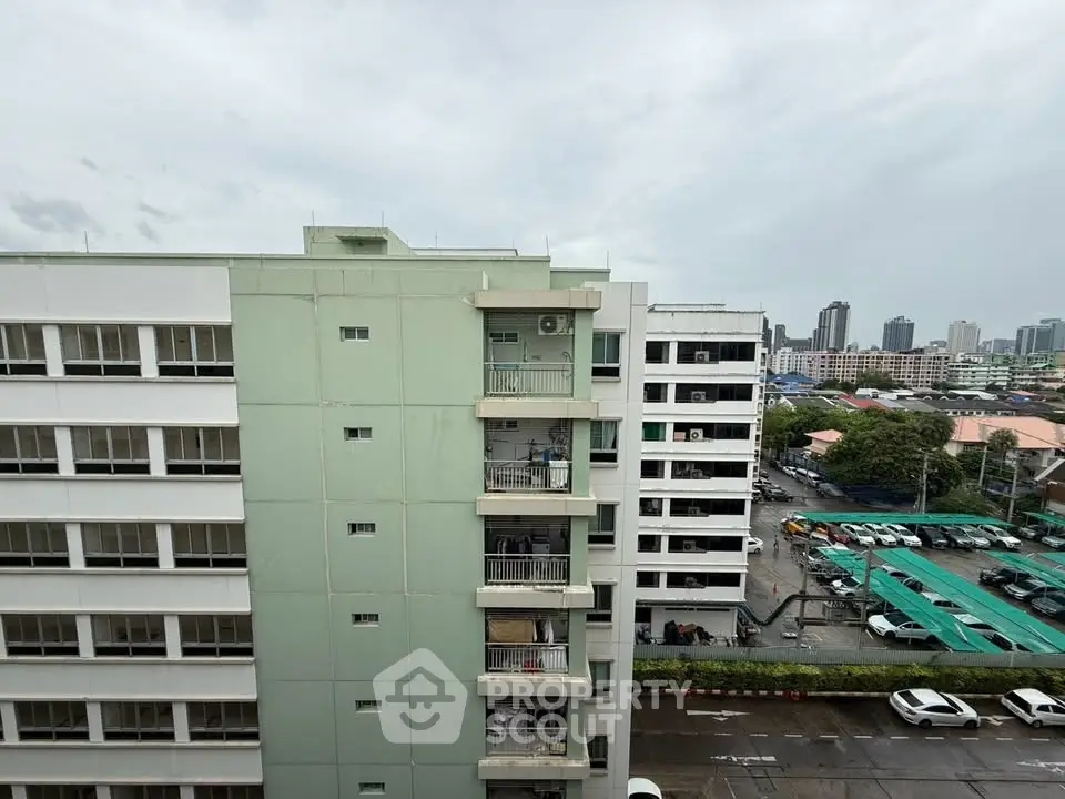 Urban apartment building with city skyline view, showcasing modern architecture and parking area.