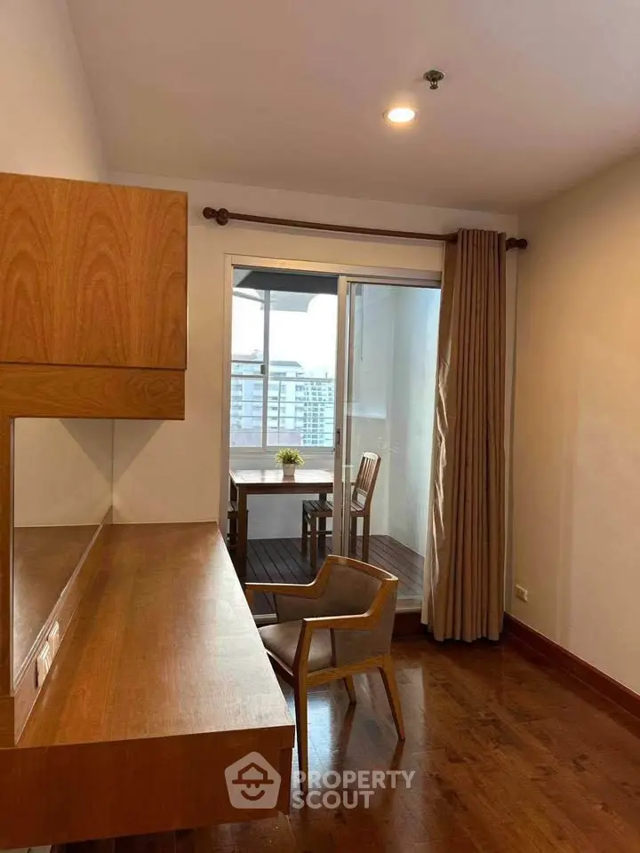 Chic study room with wooden desk and chair, leading to a cozy balcony with city views.
