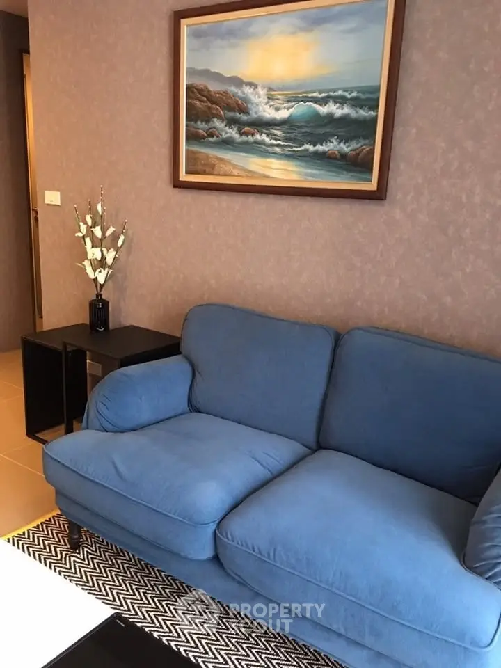 Cozy living room with blue sofa and ocean painting, perfect for relaxation.