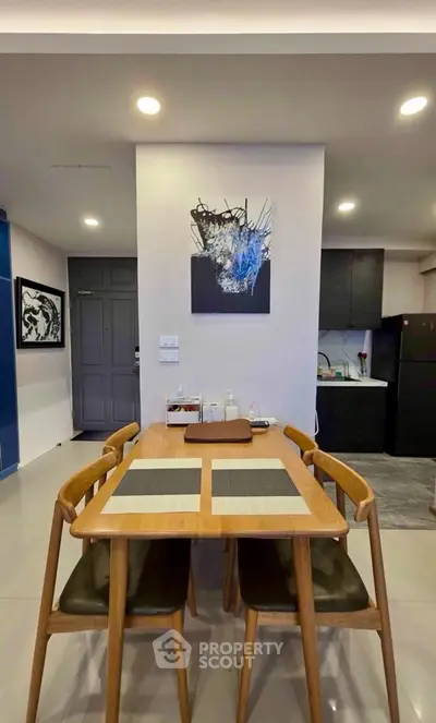Modern dining area with stylish wooden table and chairs, adjacent to a sleek kitchen with dark cabinetry.
