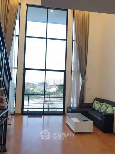 Spacious living room with high ceiling and large windows offering stunning city views.