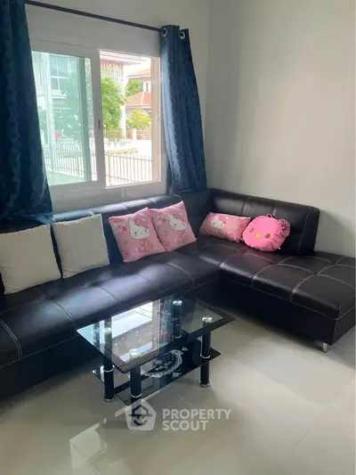 Cozy living room with modern black leather sofa and glass coffee table, bright window view.