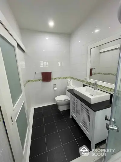 Pristine white-tiled bathroom with modern fixtures, glass shower, and stylish vanity unit, perfect for a refreshing start to the day.