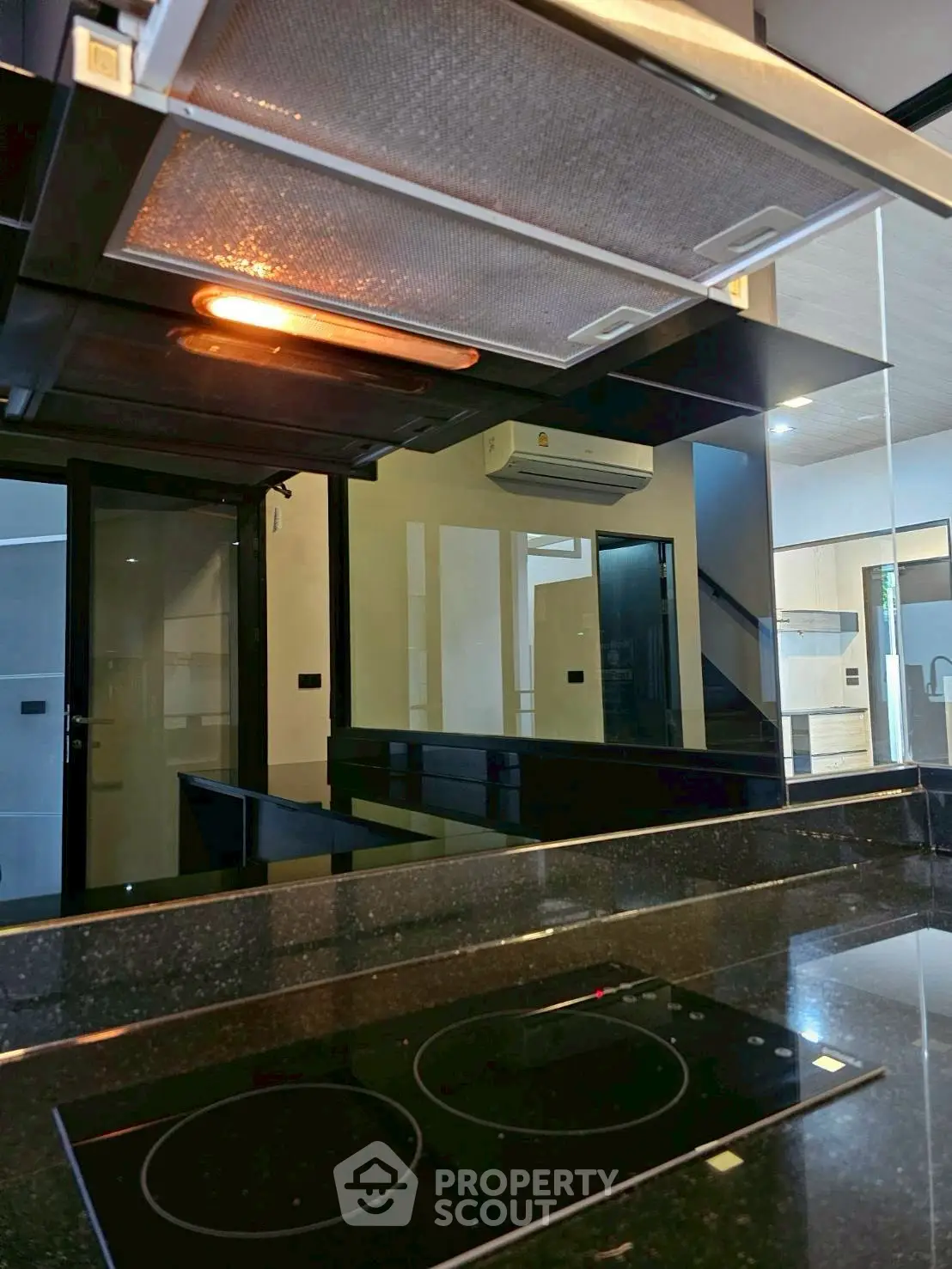 Modern kitchen with sleek black countertops and induction stove, featuring a stylish range hood and reflective surfaces.