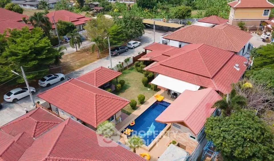 Aerial view of luxurious villa with private pool and red-tiled roofs in tropical setting.