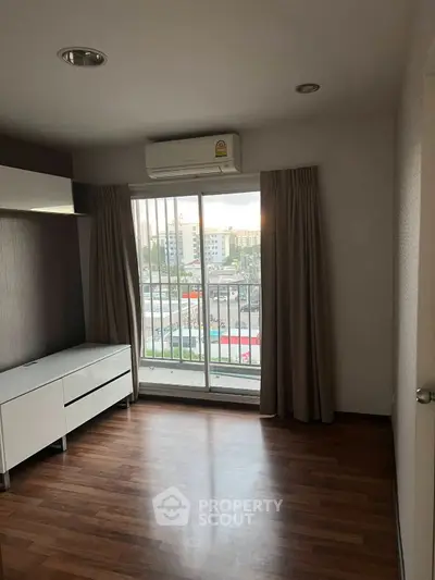 Spacious room with wooden flooring and large window offering city views
