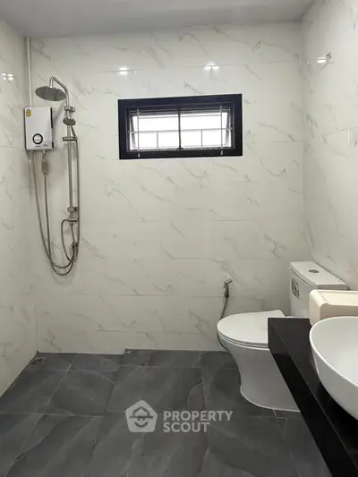 Modern bathroom with sleek fixtures and marble tiles, featuring a shower and toilet.