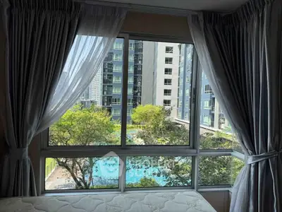Spacious bedroom with large window offering stunning pool and garden view in modern apartment complex.
