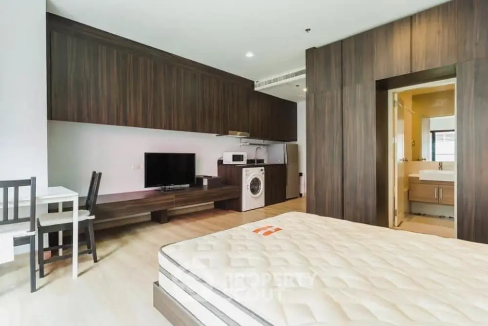 Modern studio apartment with integrated kitchen and living area, featuring a washing machine and stylish wood finishes.