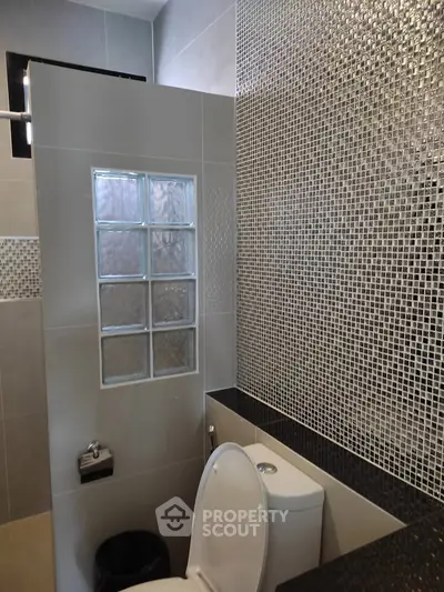 Modern bathroom with stylish mosaic tiles and glass block partition.