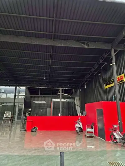 Spacious industrial-style interior with high ceilings and vibrant red accents, ideal for commercial use.