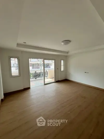 Spacious empty room with wooden flooring and balcony access in modern apartment