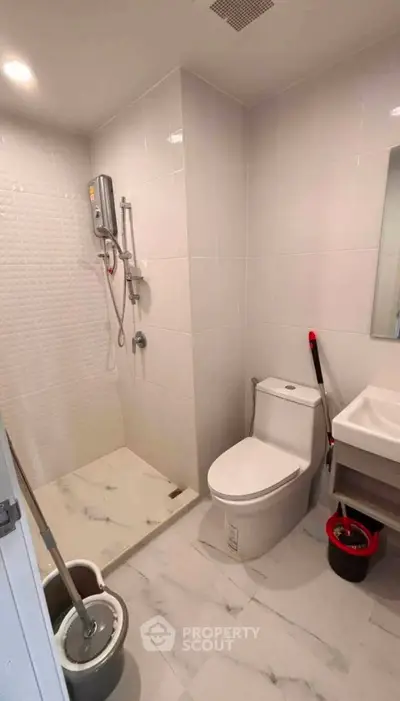 Modern bathroom with shower, toilet, and sink in sleek white design.