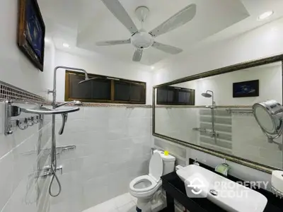 Modern bathroom with sleek fixtures and ceiling fan, featuring a large mirror and elegant lighting.