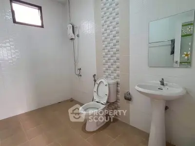 Spacious bathroom with modern fixtures and tiled walls, featuring a toilet and pedestal sink.
