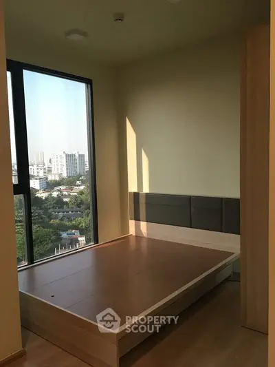 Modern bedroom with large window offering city view, featuring minimalist wooden bed frame and neutral tones.