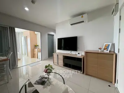 Modern living room with sleek furniture and open layout, featuring a large TV and air conditioning.