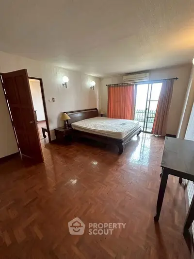 Spacious bedroom with wooden flooring and balcony access in a modern apartment.