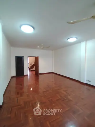 Spacious empty living room with wooden flooring and ceiling fan, ideal for customization.
