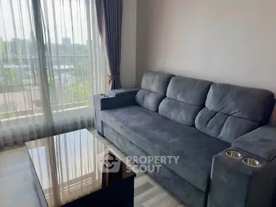 Modern living room with plush gray sofa and large window offering natural light and scenic view.