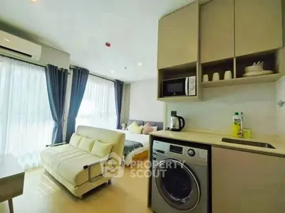 Modern studio apartment with washing machine and cozy seating area, featuring large windows and natural light.