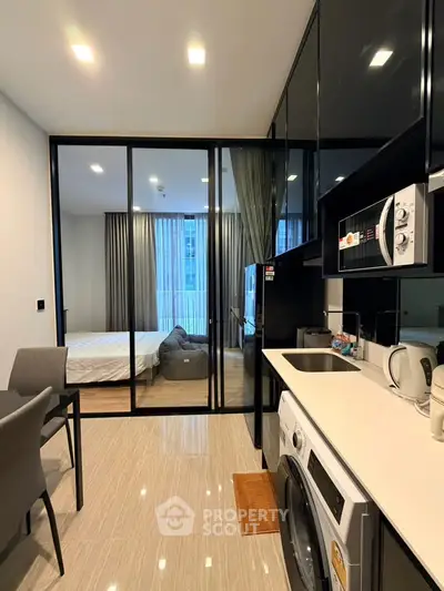 Modern apartment with sleek kitchen and cozy bedroom separated by glass partition.