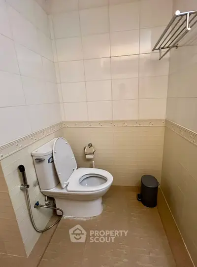 Modern bathroom with sleek toilet and tiled walls, featuring a convenient bidet spray and towel rack.
