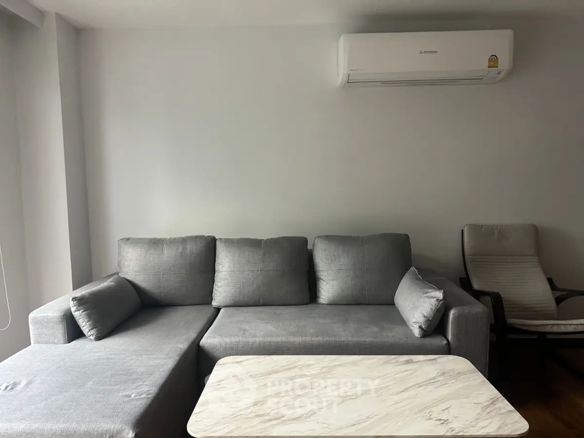 Modern living room with sleek gray sofa, marble coffee table, and air conditioning unit.
