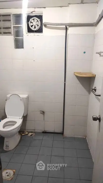 Simple bathroom with white tiles and basic fixtures, featuring a toilet and ventilation fan.