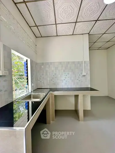 Modern kitchen with sleek countertops and tiled backsplash, featuring a large window for natural light.