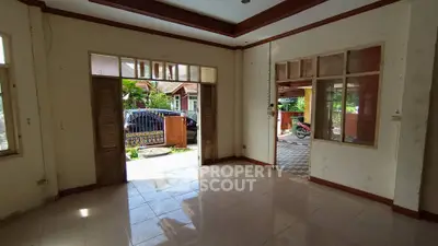 Spacious living room with open doors to a garden view, featuring tiled floors and natural light.
