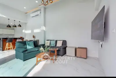 Modern living room with open kitchen, stylish furniture, and large wall-mounted TV.