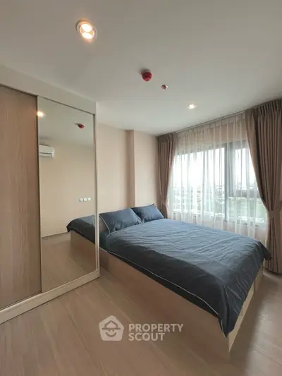 Modern bedroom with large window and mirrored wardrobe in stylish apartment.