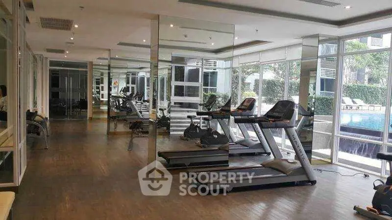 Spacious modern gym with treadmills and pool view in luxury apartment complex.