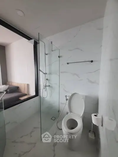 Modern bathroom with glass shower and marble tiles, adjacent to a bedroom.