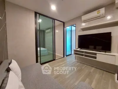 Modern living room with sleek design, featuring a large TV, air conditioning, and sliding glass doors to bedroom.