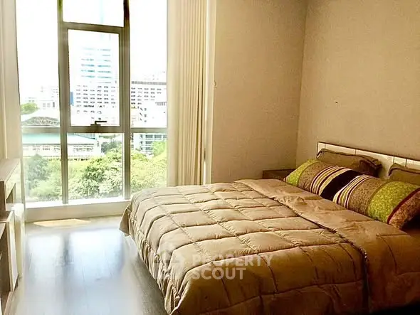 Bright bedroom with large window offering city view, featuring cozy bed and modern decor.