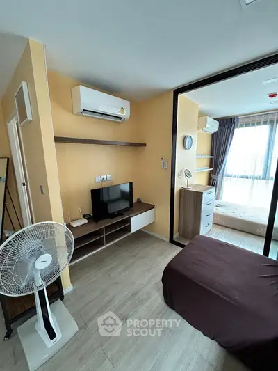 Cozy bedroom with modern air conditioning and TV setup, featuring a sliding door to a bright windowed area.