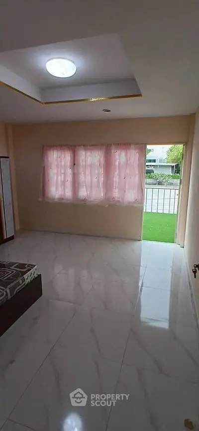Spacious living room with large window and marble flooring, offering a bright and airy atmosphere.