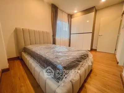 Modern bedroom with stylish bed and wardrobe, featuring warm wooden flooring and elegant curtains.