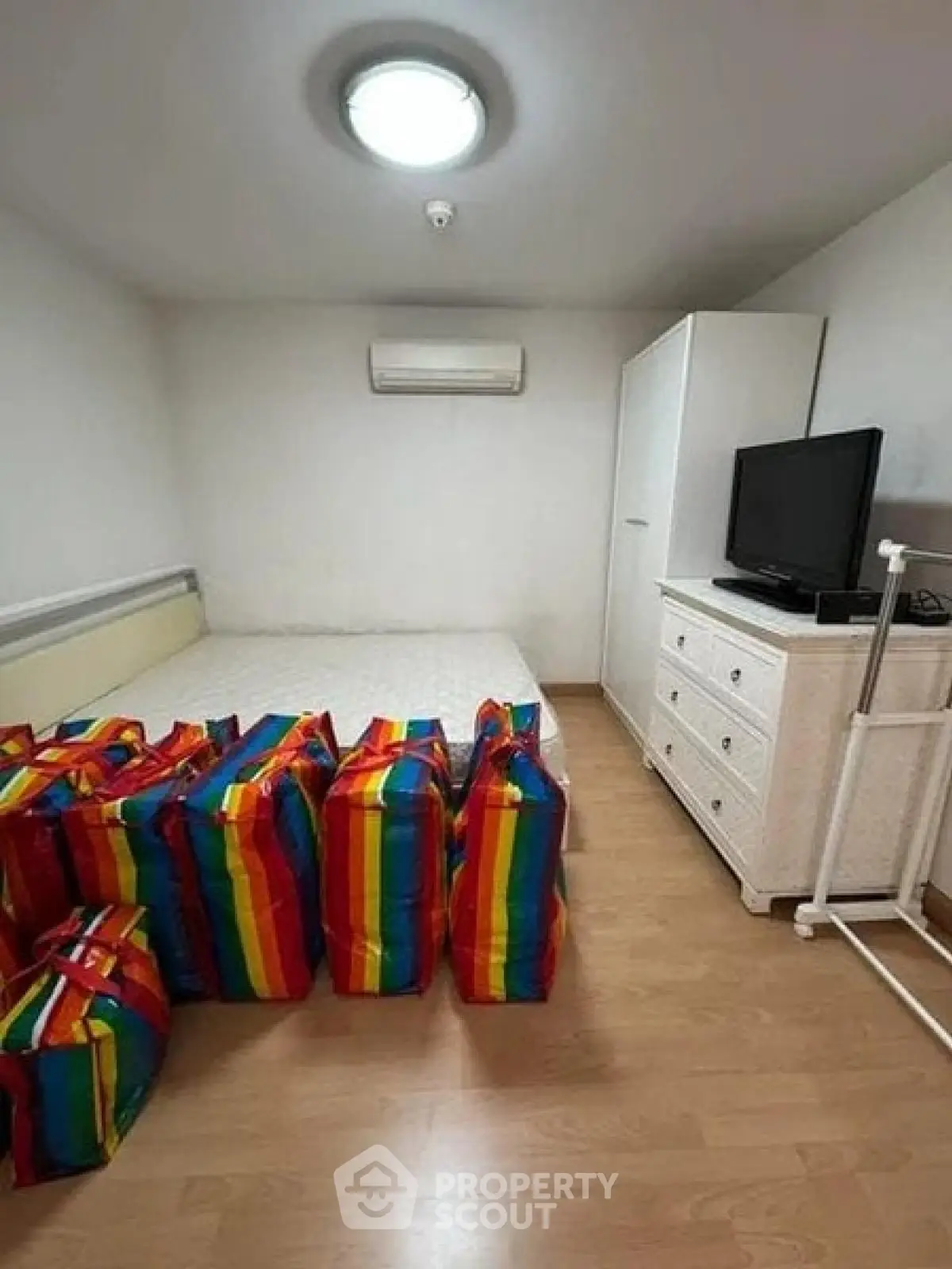 Cozy bedroom with minimalist decor and colorful storage bags, featuring a TV and air conditioning.