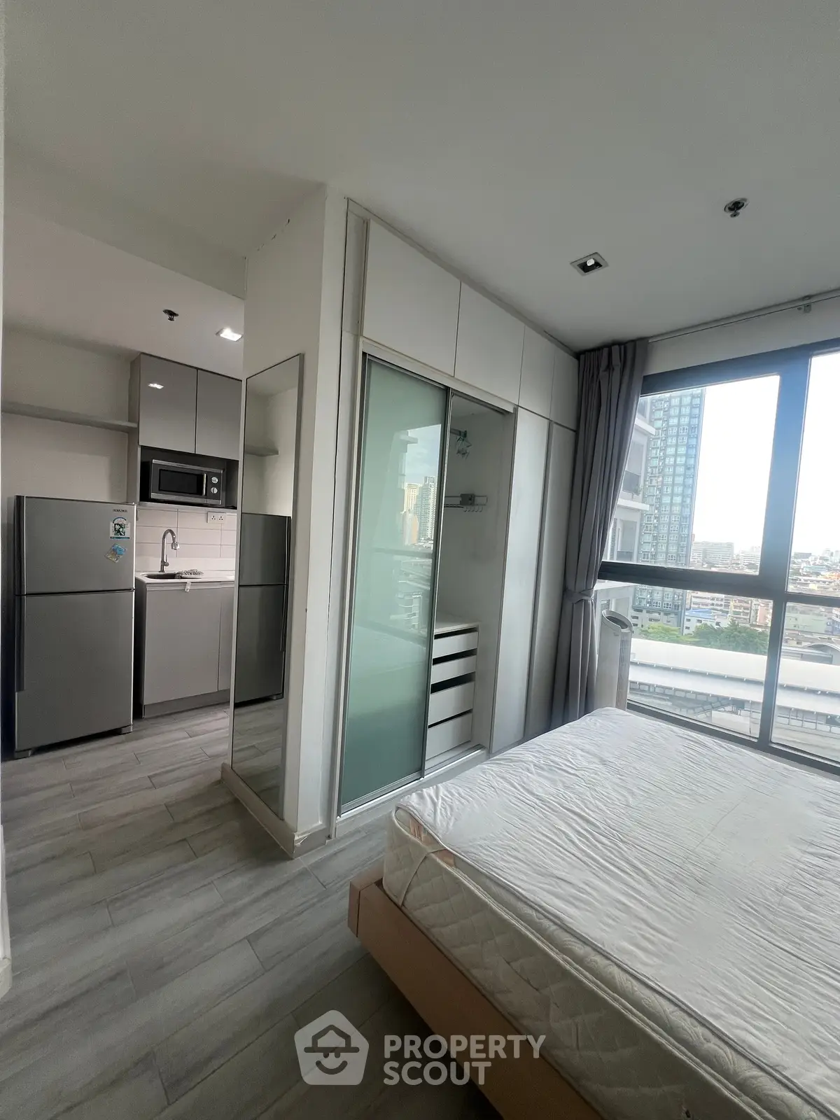 Modern apartment interior with sleek kitchen and spacious bedroom featuring large windows and city view.