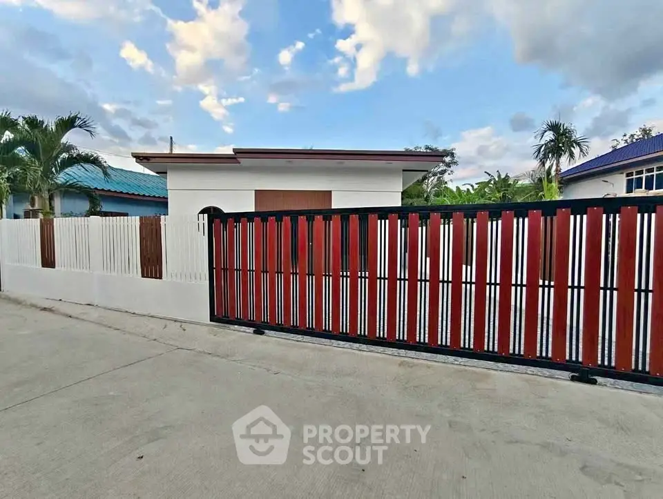 Charming modern house with stylish fence and lush palm trees under a vibrant sky.