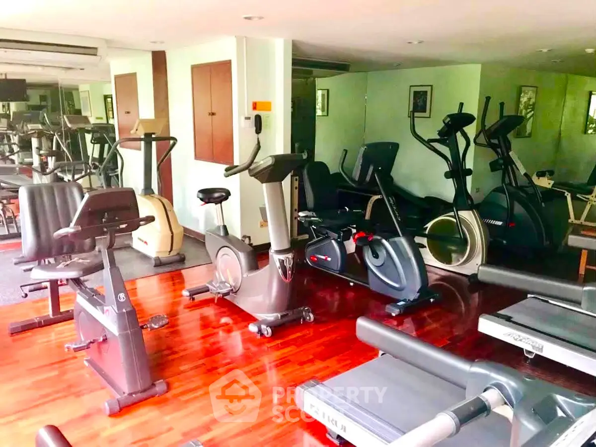 Spacious gym with modern exercise equipment and wooden flooring in a residential building.