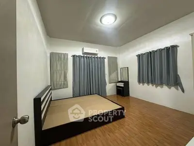 Spacious bedroom with modern bed frame and wooden flooring, featuring ample natural light and neutral decor.