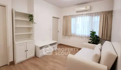 Cozy living room with white furniture and wooden flooring, featuring a large window and air conditioning.