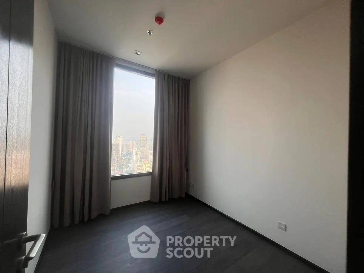 Spacious empty room with large window offering stunning city skyline view.