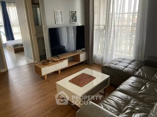 Modern living room with sleek furniture and large TV, featuring a balcony view.